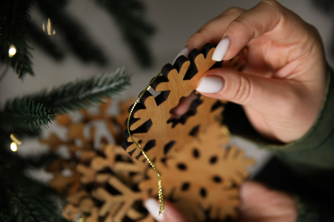 hands-holding-wooden-snowflake-ornaments-near-a-Christmas-tree-with-lights