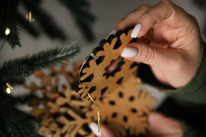 hands-holding-wooden-snowflake-ornaments-near-a-Christmas-tree-with-lights