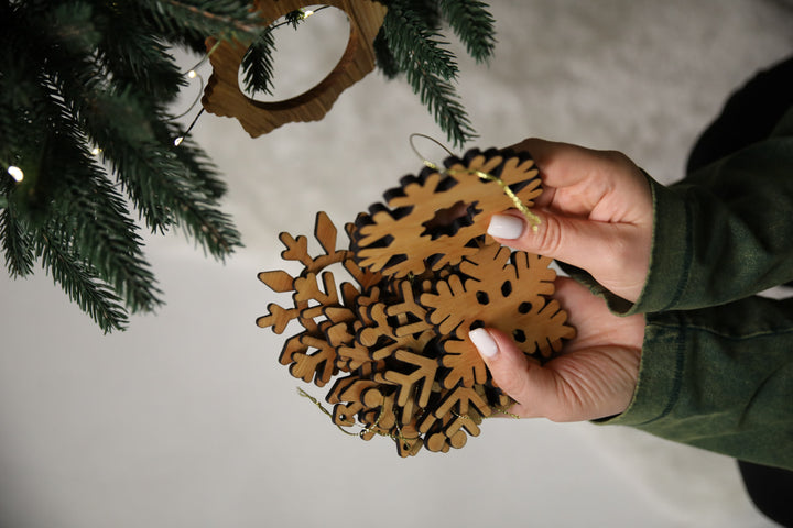 hands-holding-wooden-snowflake-ornaments-near-a-Christmas-tree-with-lights