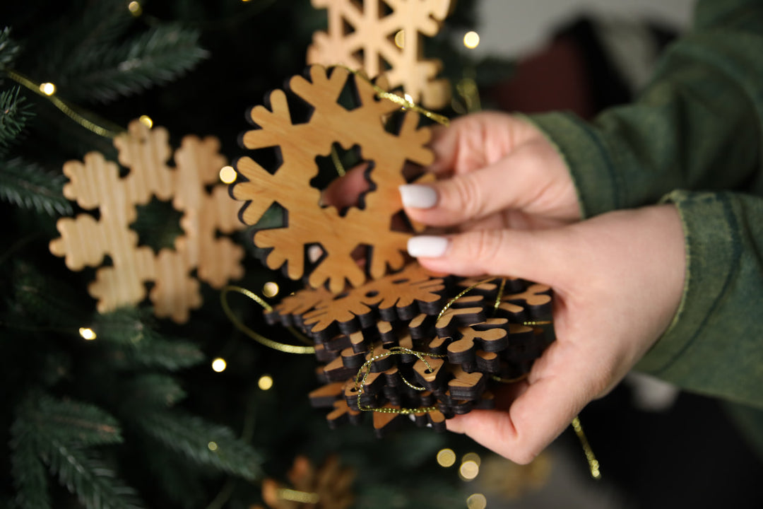 hands-holding-wooden-snowflake-ornaments-near-a-Christmas-tree-with-lights