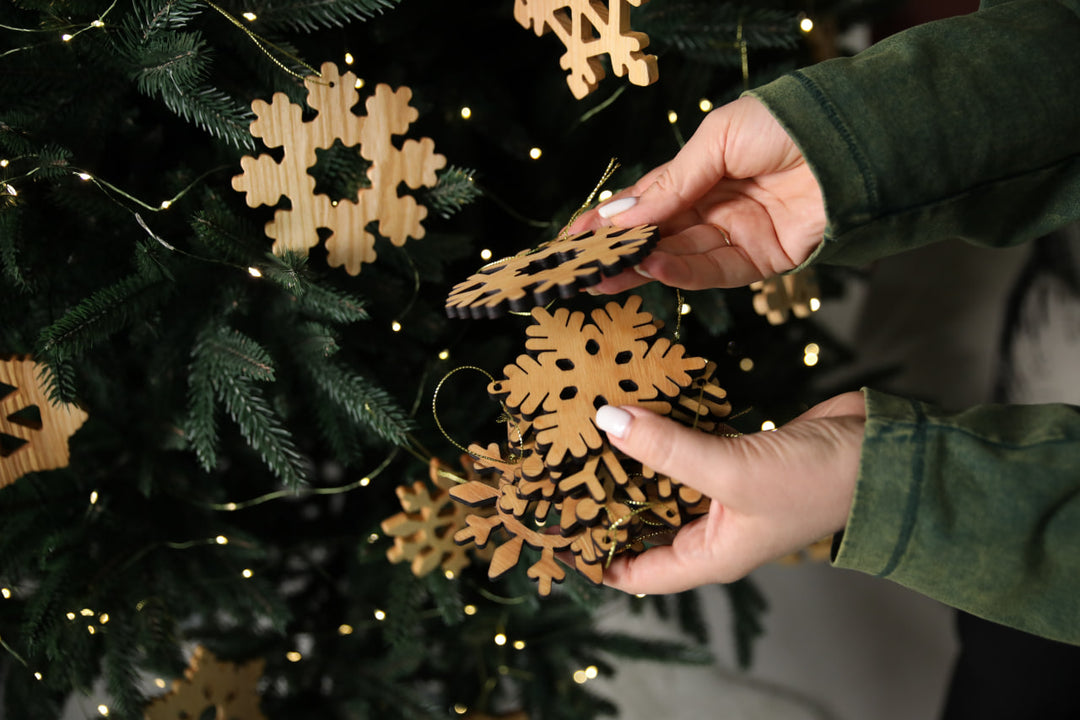 hands-holding-wooden-snowflake-ornaments-near-a-Christmas-tree-with-lights