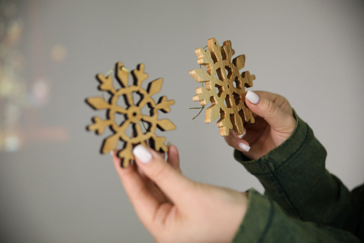 hands-holding-wooden-snowflake-ornaments-near-a-Christmas-tree-with-lights