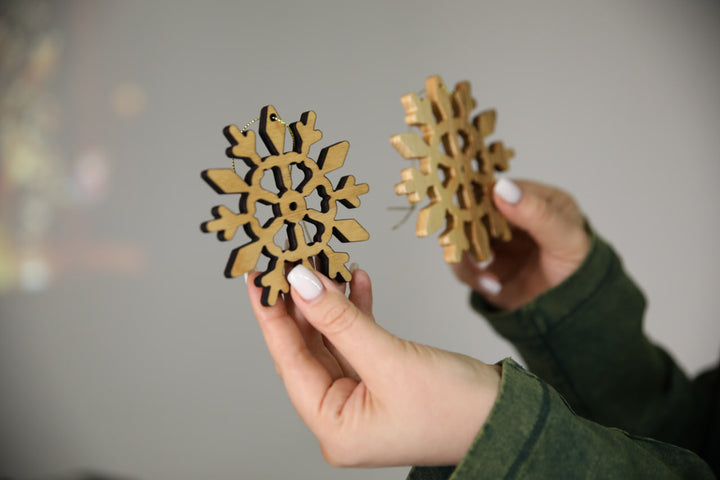 hands-holding-wooden-snowflake-ornaments-near-a-Christmas-tree-with-lights