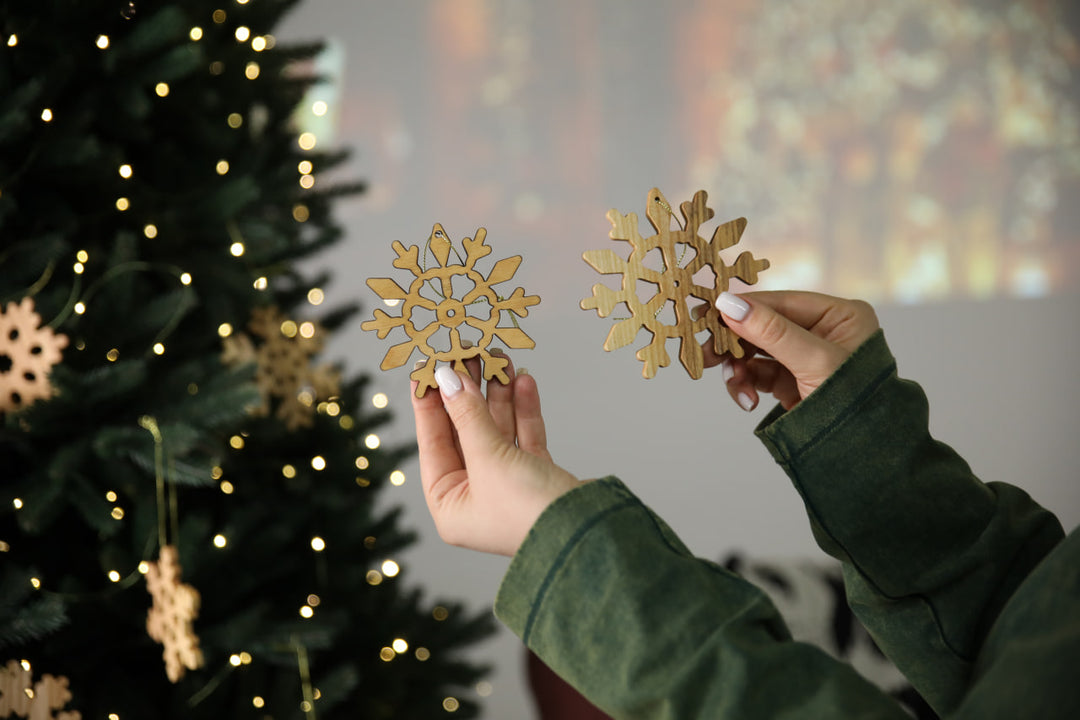 hands-holding-wooden-snowflake-ornaments-near-a-Christmas-tree-with-lights