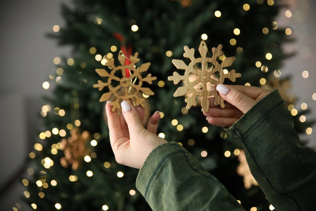 hands-holding-wooden-snowflake-ornaments-near-a-Christmas-tree-with-lights