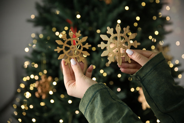 hands-holding-wooden-snowflake-ornaments-near-a-Christmas-tree-with-lights