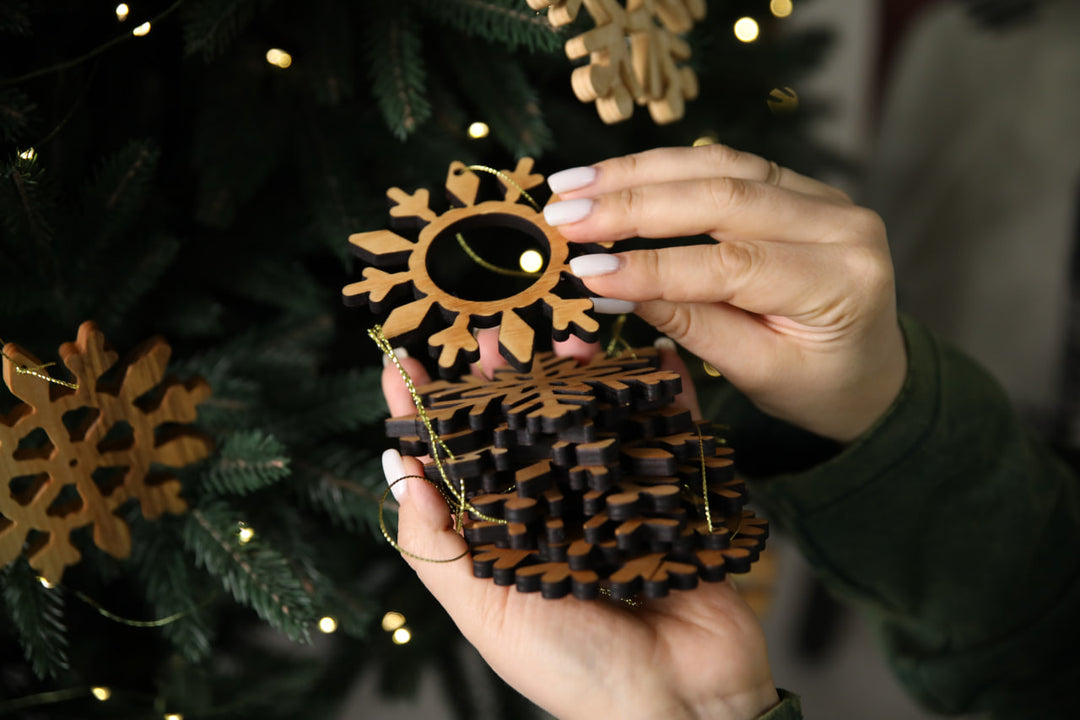 hands-holding-wooden-snowflake-ornaments-near-a-Christmas-tree-with-lights