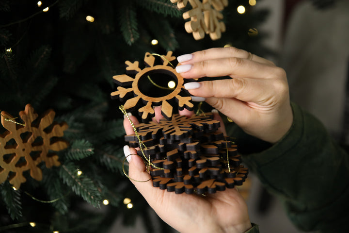 hands-holding-wooden-snowflake-ornaments-near-a-Christmas-tree-with-lights