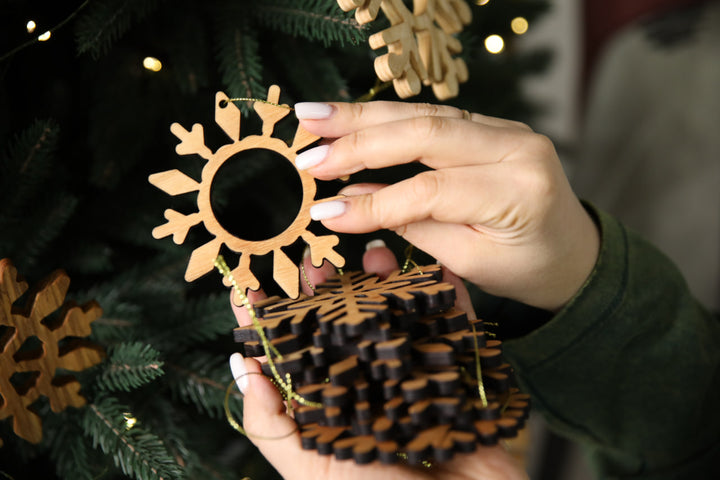 hands-holding-wooden-snowflake-ornaments-near-a-Christmas-tree-with-lights