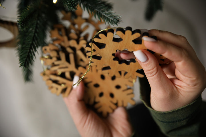 hands-holding-wooden-snowflake-ornaments-near-a-Christmas-tree-with-lights