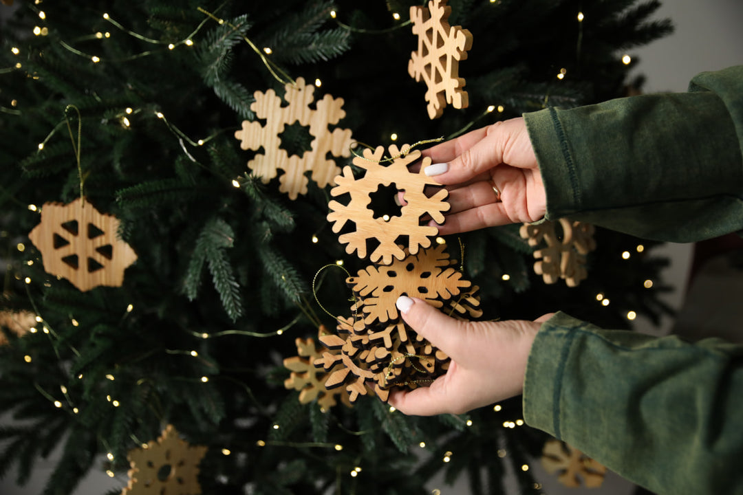 hands-holding-wooden-snowflake-ornaments-near-a-Christmas-tree-with-lights